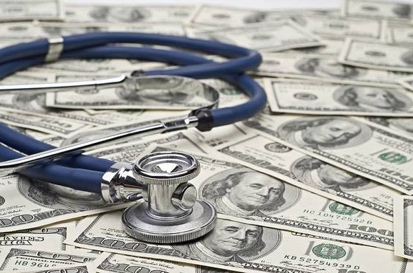 A stethoscope sits on a pile of 100-dollar bills